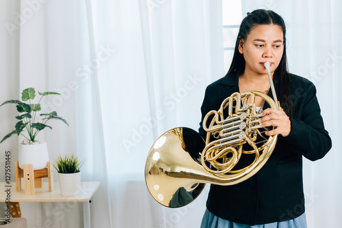 A woman wearing a black jacket holds a French horn in gold, playing it with grace and poise. The shiny instrument highlights the beauty of her musical talent.