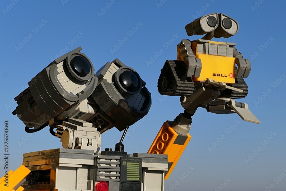 Naklejka premium LEGO Wall-E figure of robot from Disney Pixar movie of the same name holding smaller model of Wall-E in raised arm, blue skies in background.