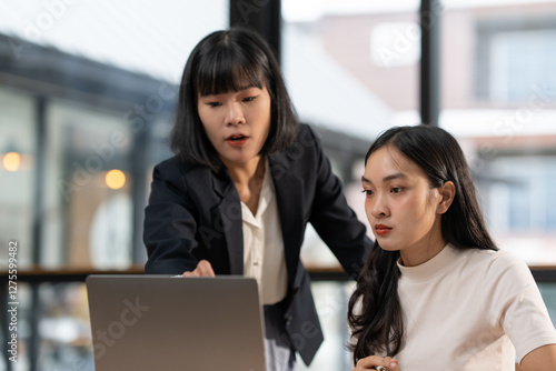 Photography Two asian businesswomen are working together on a laptop in a modern office, wit