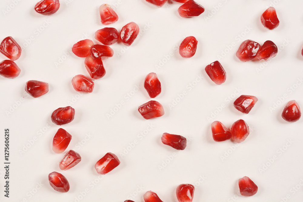 A scattered array of vibrant red pomegranate seeds glistens against a clean white background A scattered array of vibrant red pomegranate seeds glistens against a clean white background