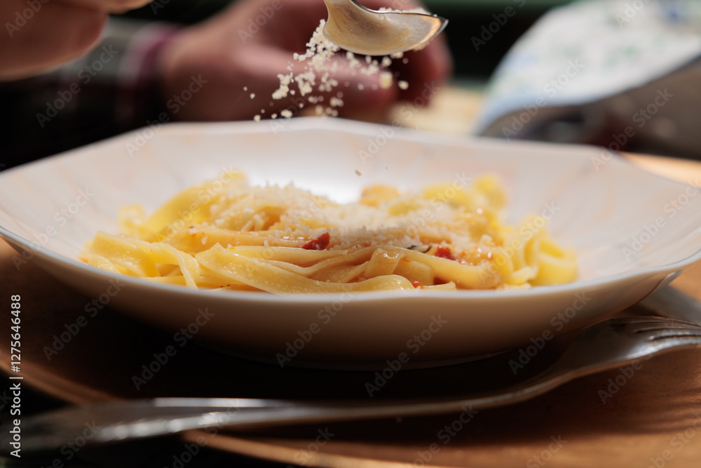 dettagli di un piatto di tagliatelle con sugo di carne mentre vengono condite con del formaggio grana grattugiato