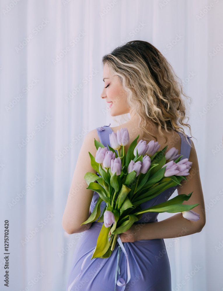 Happy blonde woman holding tulip bouquet purple flowers green leaves white background window light. Joyful girl smiling face enjoys gift. Women's day holiday, march 8, spring concept floral greeting Happy blonde woman holding tulip bouquet purple flowers green leaves white background window light. Joyful girl smiling face enjoys gift. Women's day holiday, march 8, spring concept floral greeting