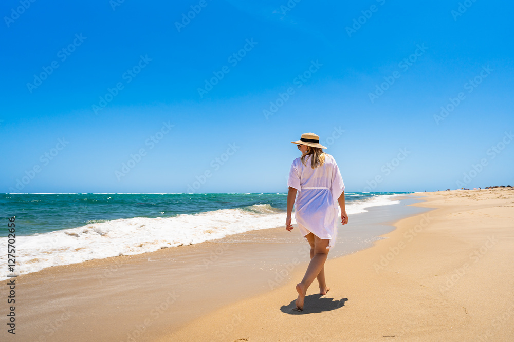 Beautiful mature woman walking on sunny sandy paradise beach on Armona island in Portugal. Travel destination - Armona beach. Back view Beautiful mature woman walking on sunny sandy paradise beach on Armona island in Portugal. Travel destination - Armona beach. Back view