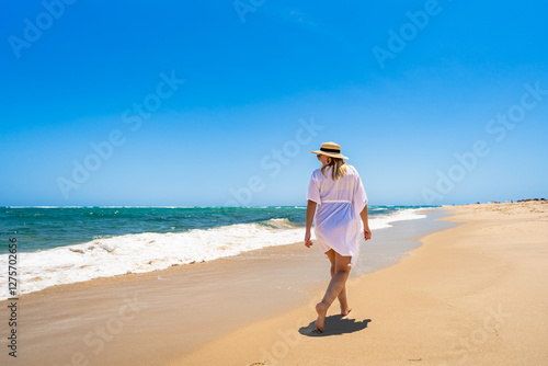 Beautiful mature woman walking on sunny sandy paradise beach on Armona island in Portugal. Travel destination - Armona beach. Back view photo