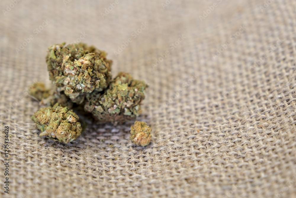A close-up of CBD cannabis buds resting on a burlap surface. The dried green and orange flowers display their trichomes and texture in detail, emphasizing their natural quality. A close-up of CBD cannabis buds resting on a burlap surface. The dried green and orange flowers display their trichomes and texture in detail, emphasizing their natural quality.