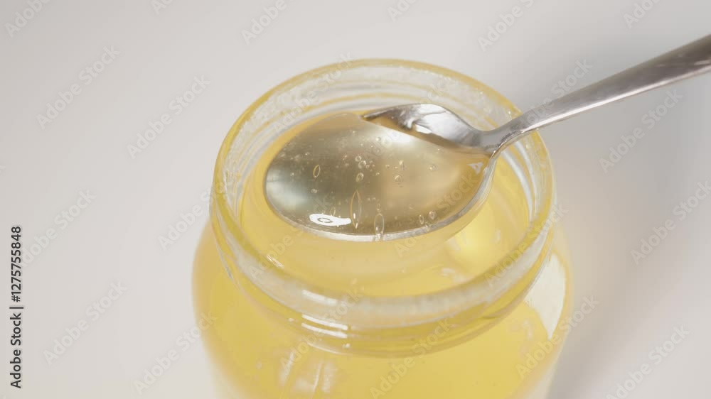 A close-up view of golden honey being poured into a glass jar, showcasing its texture and allure, with warm ambient lighting enhancing its natural beauty and appeal. A close-up view of golden honey being poured into a glass jar, showcasing its texture and allure, with warm ambient lighting enhancing its natural beauty and appeal.