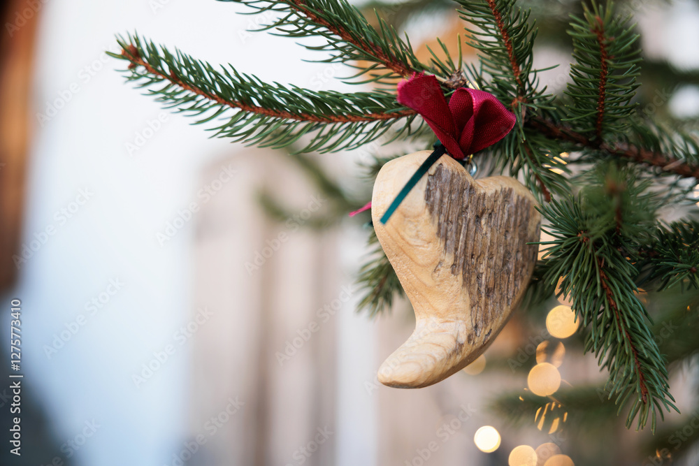 vista macro di un ramo di albero di abete con aghi verdi, decorato con un pezzo di legno a forma di cuore ed un piccolo nastro rosso in tema natalizio