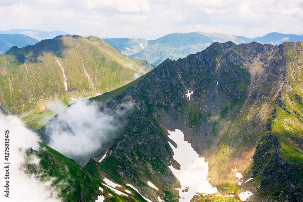 clouds in the mountains. remote recreation. landscape of transylvania alps on a sunny summer day. scenery with steep rocky slopes with grass and snow. beautiful nature background. majestic elevation