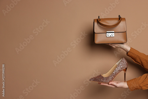 Woman showing stylish bag and glitter high-heeled shoe on beige background, closeup. Space for text photo