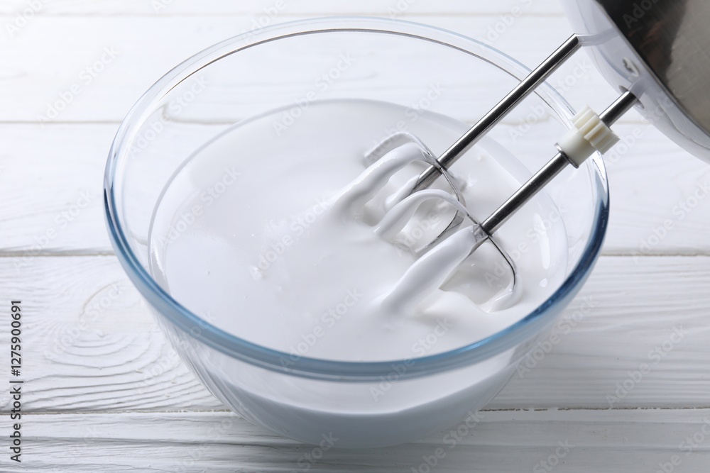 Mixing whipped cream with hand mixer in bowl on white wooden table, closeup Mixing whipped cream with hand mixer in bowl on white wooden table, closeup