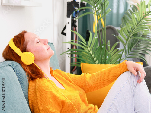 Woman with yellow headphones and a glass of wine sitting on the sofa at home and listening to music or podcast. music and relaxation