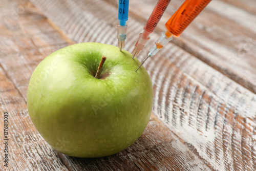 GMO concept. Green apple with syringes on rustic wooden table, closeup