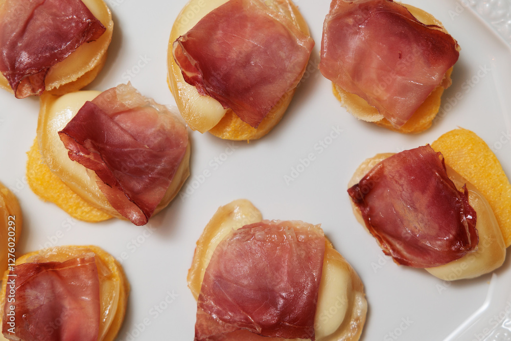dettaglio di un piatto visto dall'alto con degli antipasti a base di fette rotonde di polenta, scamorza affumicata e prosciutto crudo