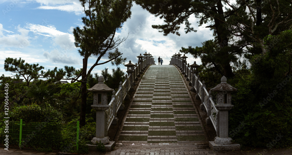 Majestic Stone Bridge with Ornate Lanterns and Two Silhouetted Figures Under Vast Sky in Jeju Island Majestic Stone Bridge with Ornate Lanterns and Two Silhouetted Figures Under Vast Sky in Jeju Island