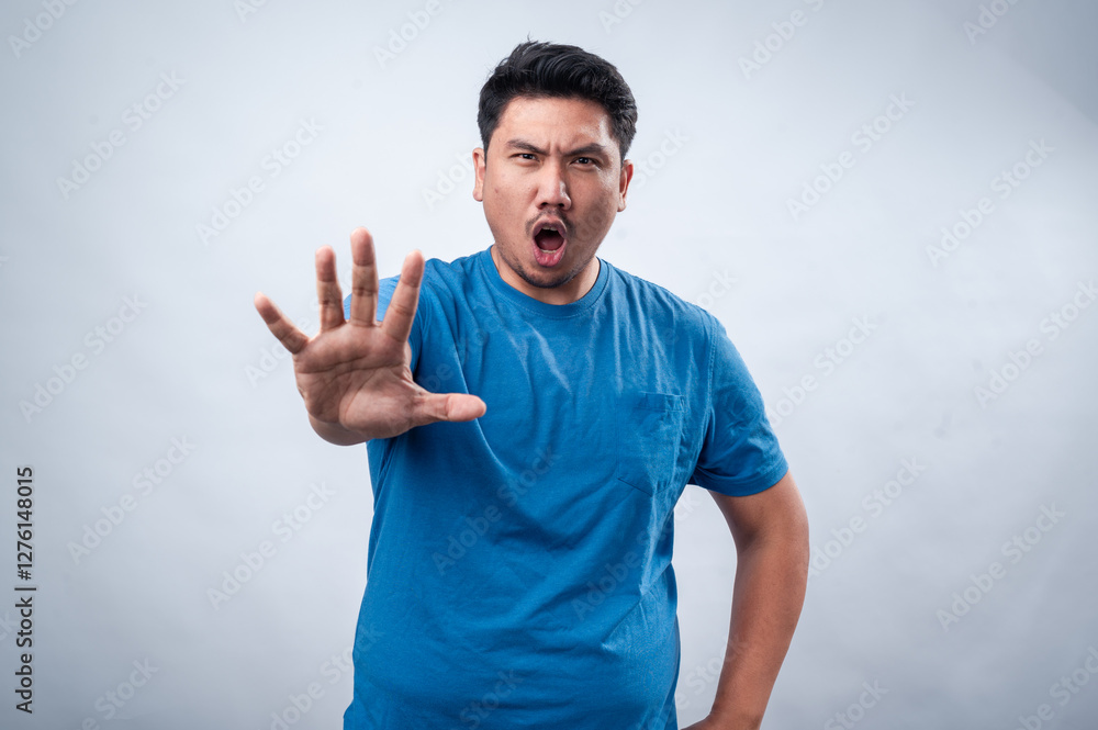 Fototapeta premium An Asian man in a blue t-shirt extends his hand forward with his palm open in a commanding 