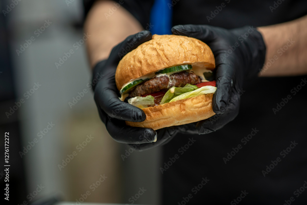 Chef in black gloves preparing gourmet burgers with fresh vegetables and sauce and cutlet in fast food restaurant