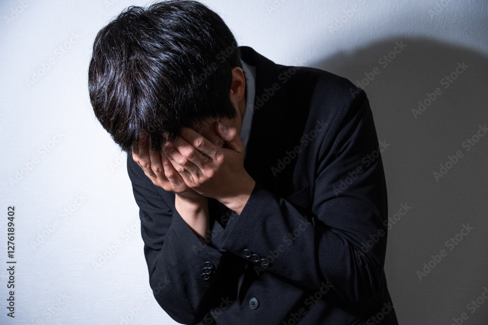 顔を手で隠すビジネスマンとスポットライト