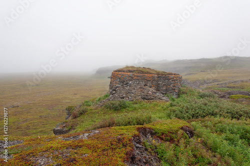 Foggy morning in the tundra. Old abandoned stone pillbox on the hill. Cape Kekursky, Rybachy Peninsula, Murmansk region, Northern Russia photo