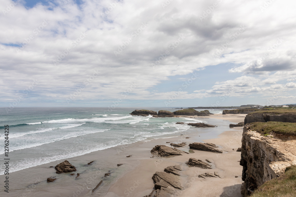 A scenic coastal landscape featuring a sandy beach, rugged rock formations, and ocean waves under a partly cloudy sky. A peaceful and natural seaside view A scenic coastal landscape featuring a sandy beach, rugged rock formations, and ocean waves under a partly cloudy sky. A peaceful and natural seaside view
