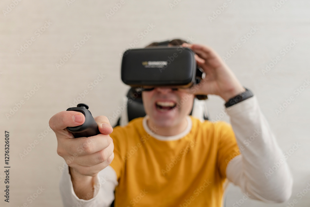 Young smiling man in VR glasses playing video game with joystick, siting on the couch while having virtual reality experience Young smiling man in VR glasses playing video game with joystick, siting on the couch while having virtual reality experience