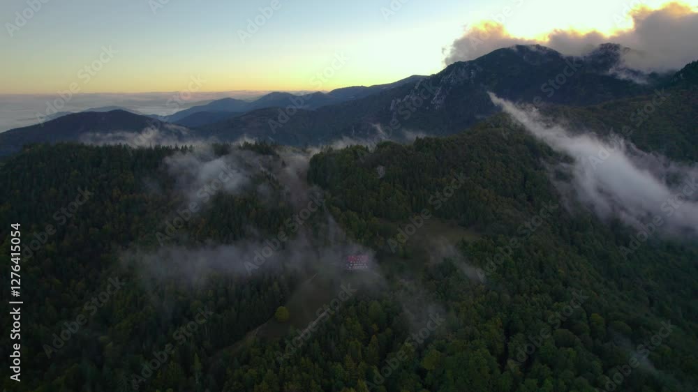 A mountain hut in a beautiful mountain surrounded by forest and trees, morning fog, inversion, low clouds form a magical panorama. Drone footage, Slovakia, Malá Fatra. A mountain hut in a beautiful mountain surrounded by forest and trees, morning fog, inversion, low clouds form a magical panorama. Drone footage, Slovakia, Malá Fatra.