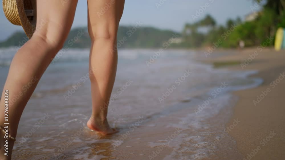 Barefoot woman strolls on sandy shore, waves wash over her feet, holding straw hat. Leisure walk on tropical beach, feeling of relaxation, summer travel vibe. Seaside vacation, freedom concept. Barefoot woman strolls on sandy shore, waves wash over her feet, holding straw hat. Leisure walk on tropical beach, feeling of relaxation, summer travel vibe. Seaside vacation, freedom concept.