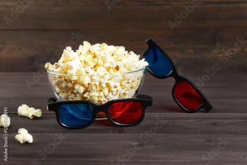 A bowl of popcorn popcorn and 3D glasses for watching movies with friends in an online cinema on a dark wood background. photo