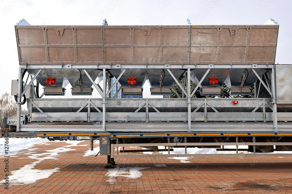 Large metal containers with red vibrators and shakers rest on a trailer in a snowy yard on a cold winter day.