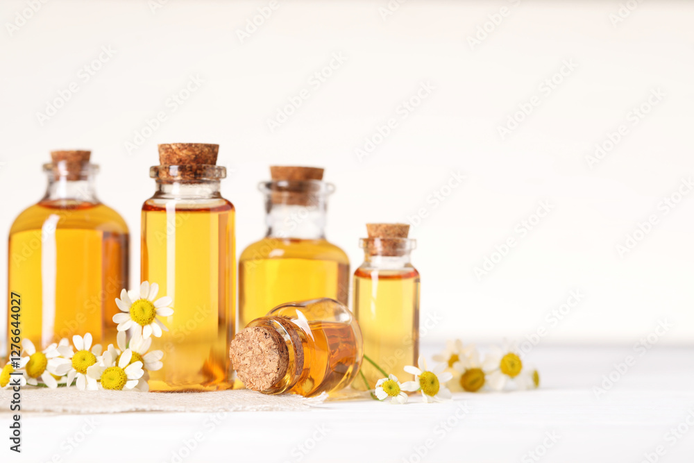 Bottles of essential oil and chamomile flowers on white wooden table, closeup. Space for text Bottles of essential oil and chamomile flowers on white wooden table, closeup. Space for text
