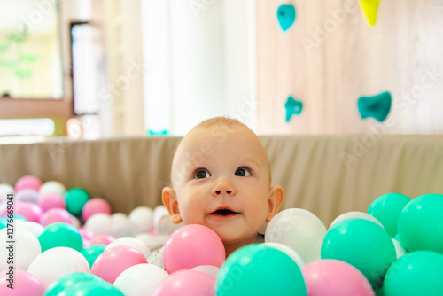 A baby boy playing in a children's ball pit with plastic balls