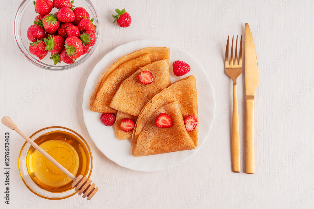 Top view of traditional sweet folded crepe french dessert or sweet blini tasty snack made from batter served on plate with red strawberries on white wooden table with bowl of honey, fork and knife Top view of traditional sweet folded crepe french dessert or sweet blini tasty snack made from batter served on plate with red strawberries on white wooden table with bowl of honey, fork and knife