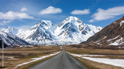 Scenic road trips in the USA depend on weather. A scenic road leads through a snowy valley, flanked by majestic mountains under a clear blue sky. photo