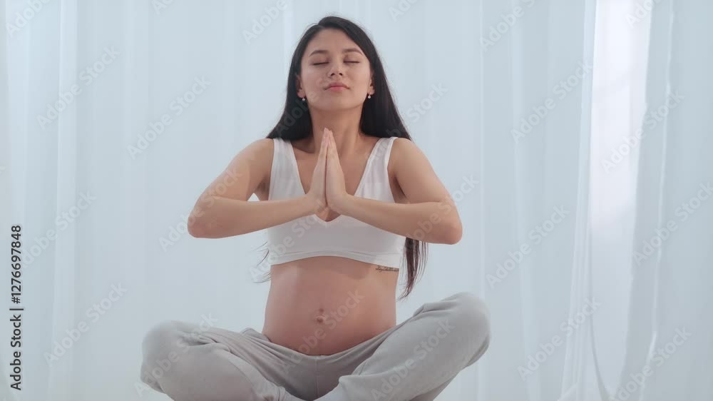 Young happy Asian pregnant woman posing in studio with white curtains in background Young happy Asian pregnant woman posing in studio with white curtains in background