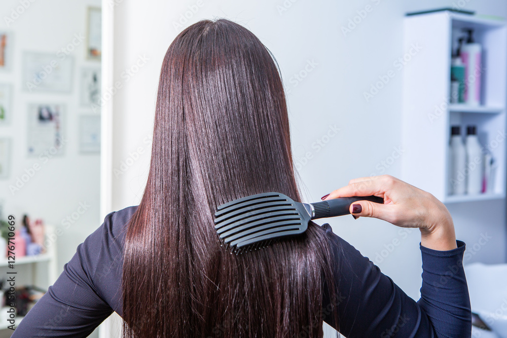 Fototapeta premium woman combs her beautiful brunette hair at the beauty salon. Healthy hair