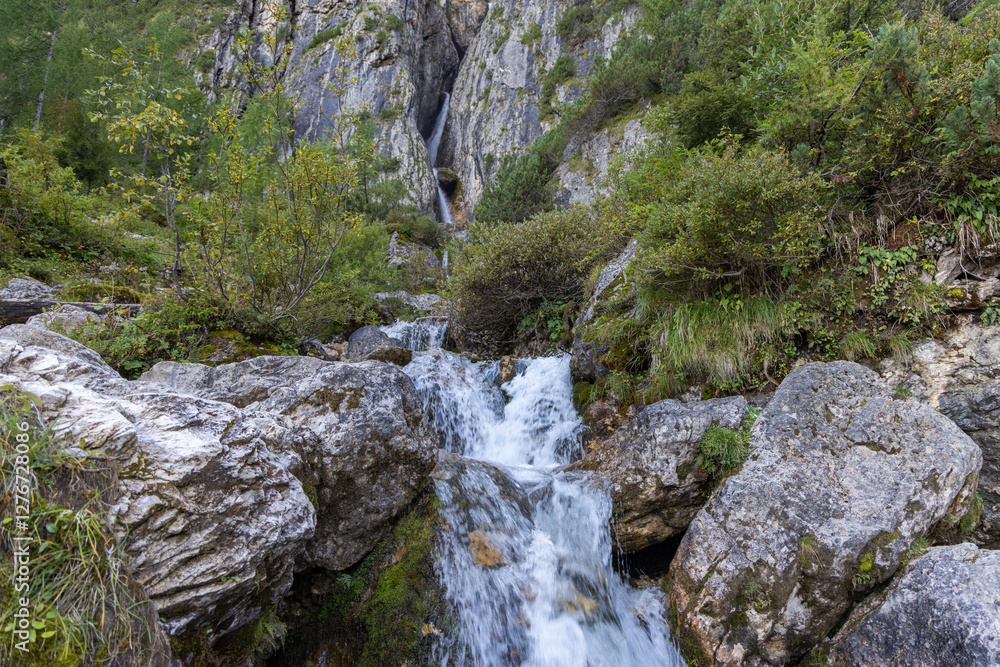 Pisciadu waterfalls in the Dolomites cascade over mossy rocks, surrounded by dense alpine vegetation in a natural mountain setting Pisciadu waterfalls in the Dolomites cascade over mossy rocks, surrounded by dense alpine vegetation in a natural mountain setting