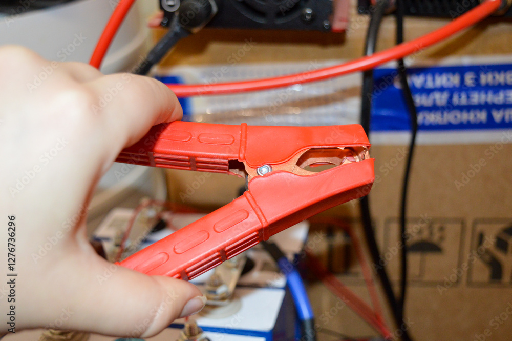 Obraz premium hand holding red jumper cable clamp battery system connected wiring setting technical electrical environment energy storage automotive repair off-grid power solutions charging upkeep renewable energy 