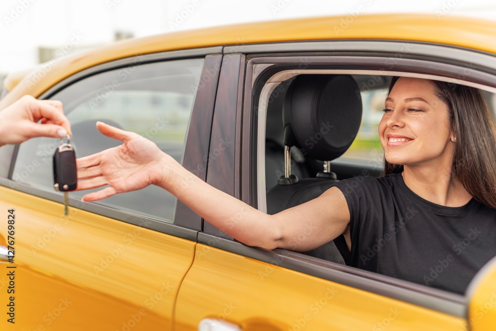 A smiling woman sitting in a yellow car receives a set of keys from another person, symbolizing a car purchase, rental, or ownership transfer.