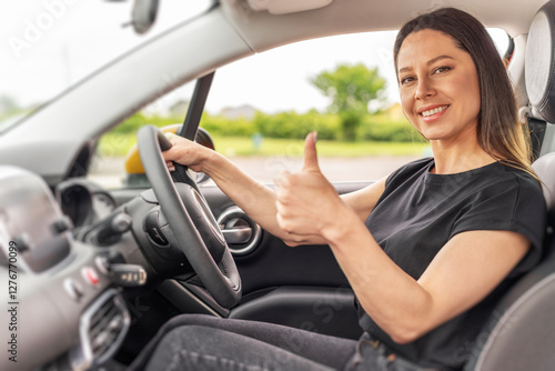 Obraz na płótnie A young woman with long brown hair and a bright smile sits in the driver's seat of a yellow car, giving a thumbs-up gesture through the open window with a confident and positive expression. w salonie