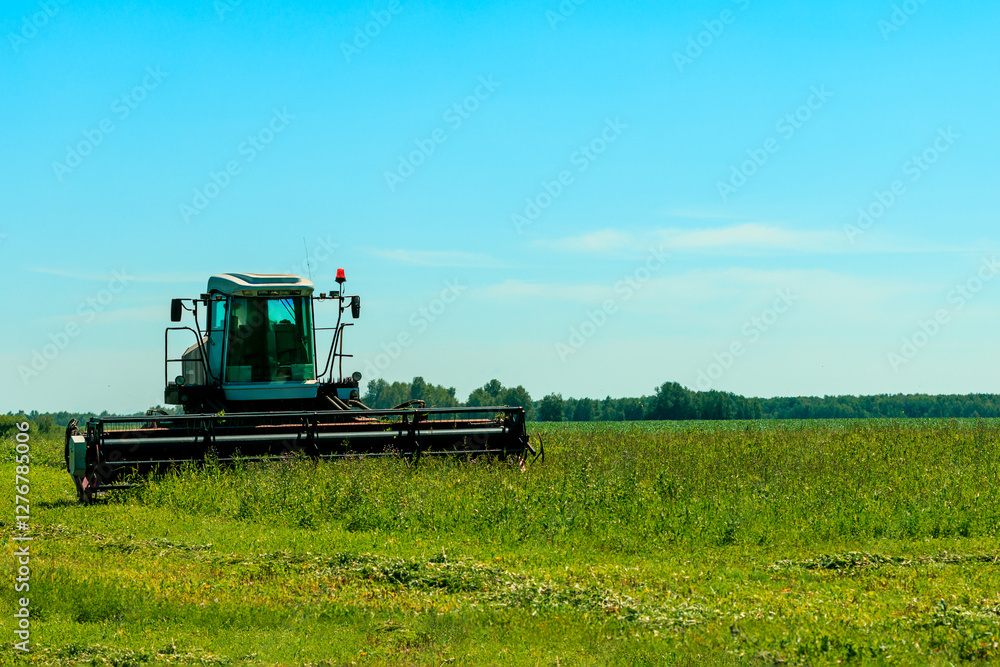 Fototapeta premium A tractor is driving through a field of grass