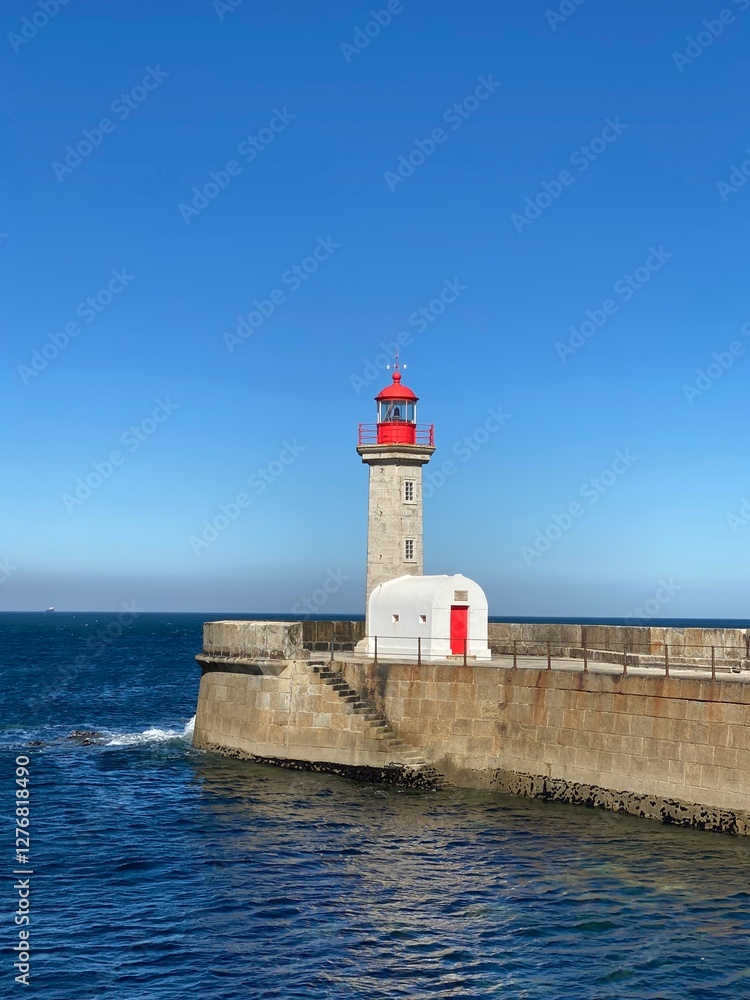 Red-topped tower with white building on a breakwater. Blue sea and clear sky. Coastal landmark and travel. Lighthouse. Red-topped tower with white building on a breakwater. Blue sea and clear sky. Coastal landmark and travel. Lighthouse.
