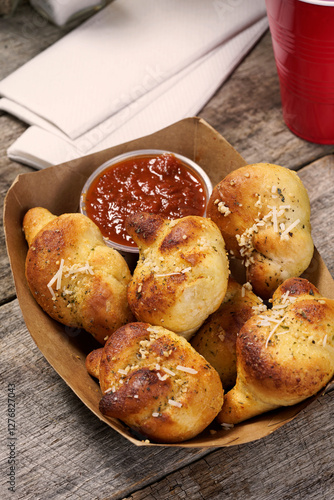 Italian garlic bread knots with marinara dipping sauce in food basket on rustic wood surface