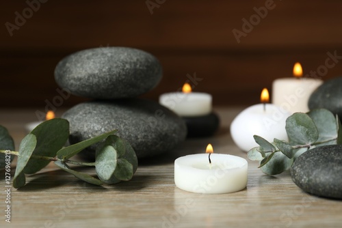 Beautiful composition with burning wax candles, stones and eucalyptus on the tablе photo