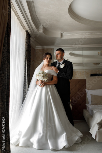 couple in wedding clothes. In the background you can see part of the room with a table lamp and a painting on the wall. photo