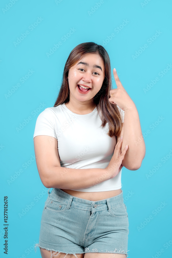 Cheerful young woman pointing upwards, having a bright idea against a vibrant blue background, expressing inspiration and creativity. Cheerful young woman pointing upwards, having a bright idea against a vibrant blue background, expressing inspiration and creativity.
