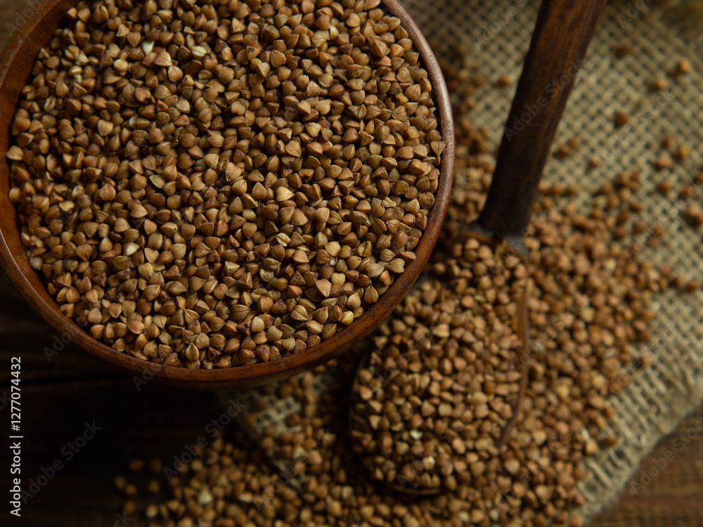 Organic buckwheat groats in a wooden bowl with a spoon on a linen napkin on a wooden table. Organic buckwheat groats in a wooden bowl with a spoon on a linen napkin on a wooden table.