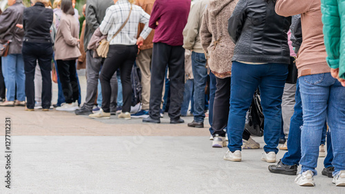 Group of anonymous diverse people standing in queue outdoors, long line of men and women, rear view. Concept of waiting, patience, urban life