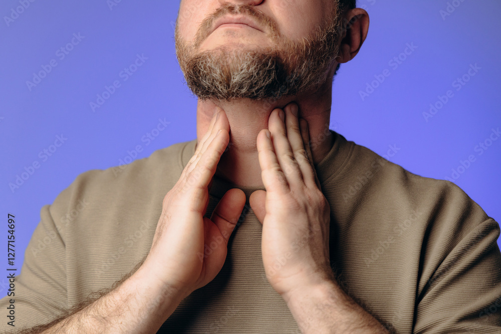 Fototapeta premium A man has a sore throat and neck due to a cold. The man holds his hand to his throat. He experiences discomfort when swallowing. The concept of viral diseases