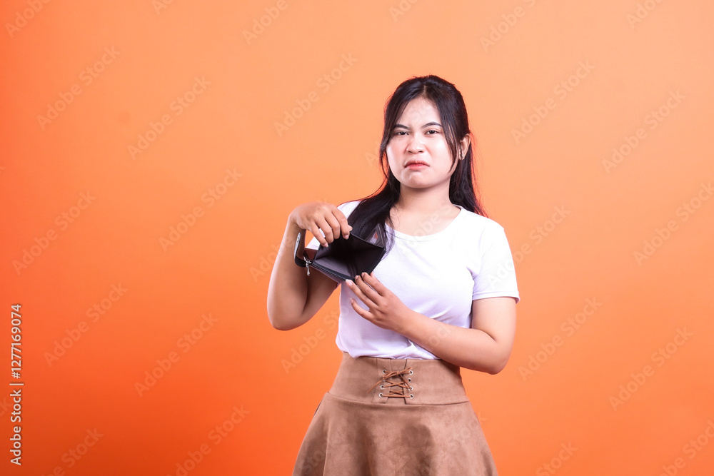 Obraz premium A woman shows an empty wallet in front of orange background, symbolizing financial difficulty