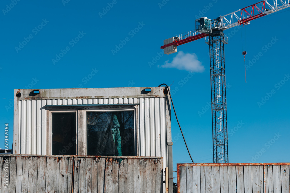 Fototapeta premium Weathered Construction Container and Tower Crane Against a Clear Blue Sky