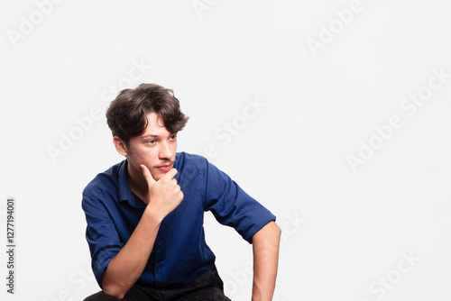 Young handsome student with black hair and blue shirt, sitting, looking seriously at the camera. Isolated on white background. Confident person.